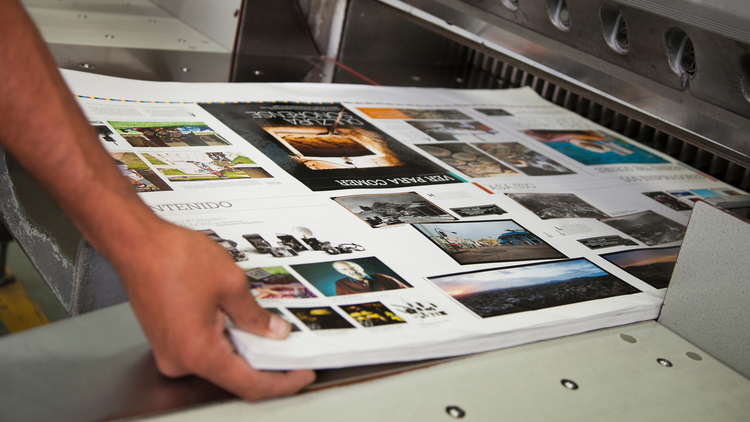 A stack of paper fresh out of the printer. A hand is in the process of picking them up.