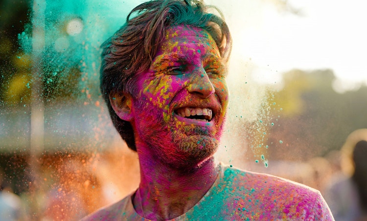 En AI-genererad bild av en mans ansikte täckt av mångfärgat Holi-pulver.