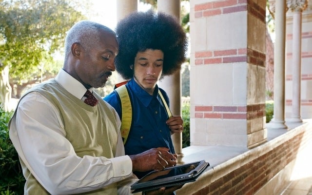 A professor looking over a letter of recommendation with a student on a tablet in between classes