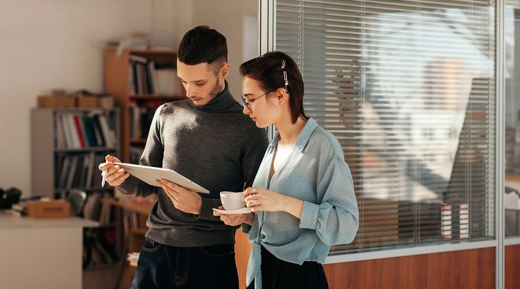 A young man and young woman standing and reviewing a wholesale contract on a tablet together.