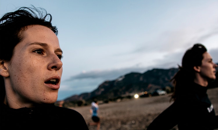 A close-up shot of two women running through a field with hills in the background.