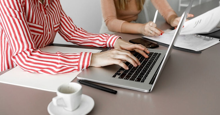 Two people sitting next to each other with one person using their laptop and another reviewing a paper document