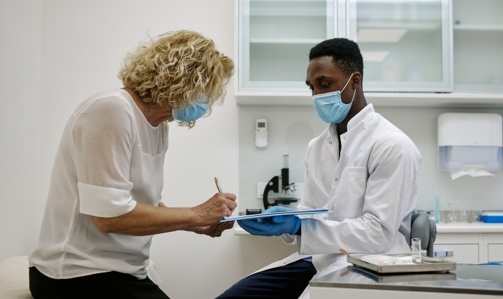 A lab tech holds a clipboard for a patient to sign a informed consent form before collecting a sample