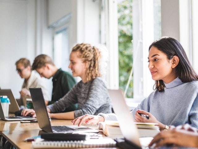 A photo of college students sitting together in a classroom using their laptops