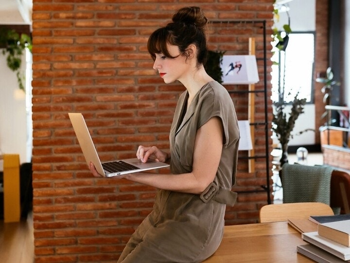 A person leaning against their desk reviewing content on their laptop
