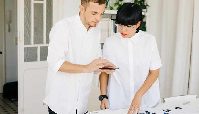 Two small business owners reviewing a digital contract while working over a table of product components.