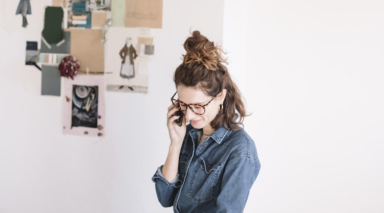 Brunette woman in a denim shirt and turtleshell glasses talking on her phone