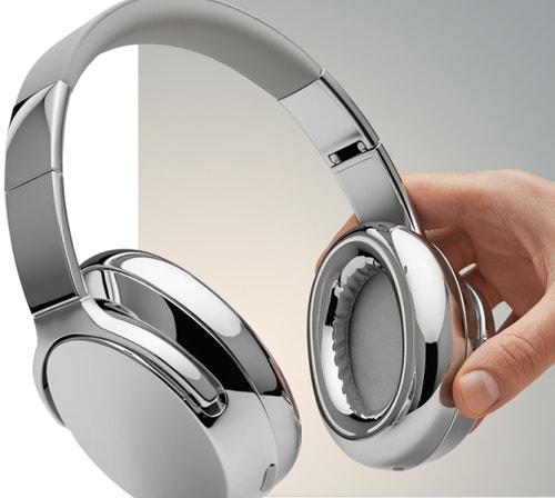 Рука тримає пару елегантних сріблястих навушників на нейтральному фоні.