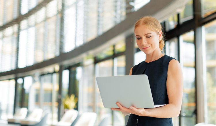 Woman stands in sunny office and uses a laptop to remove password from PDF.