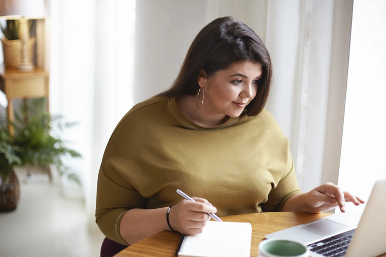 A woman writing on a legal pad while using her computer