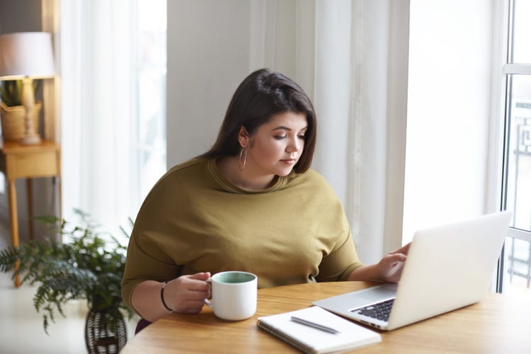 A woman in a living room uses her laptop to learn how to delete a blank page in Word.