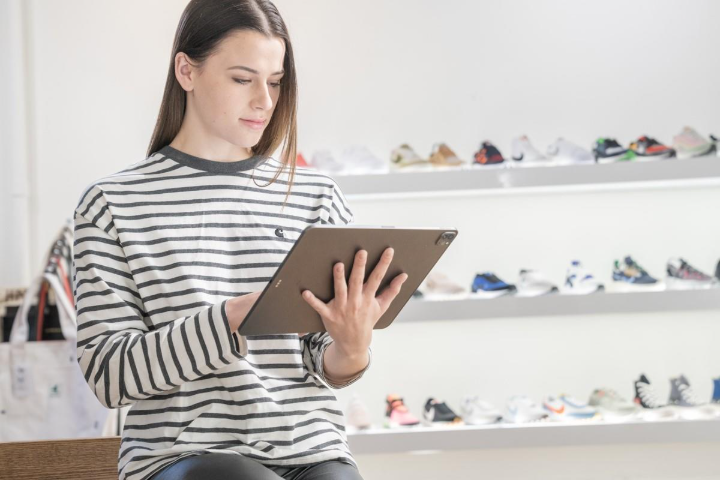 Person wearing a striped shirt in front of an athletic shoe display working on a 50 30 20 budget template PDF on a tablet.