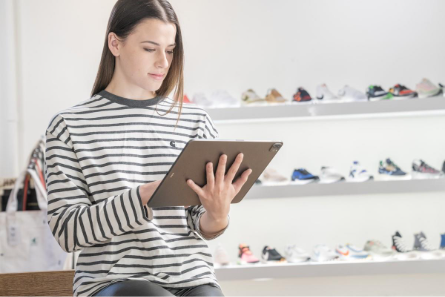 Person wearing a striped shirt in front of an athletic shoe display working on a 50 30 20 budget template PDF on a tablet.