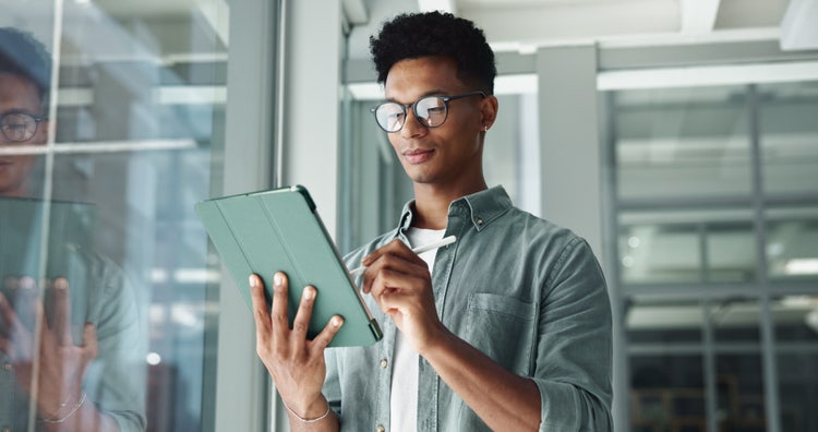 A man stands in an office holding an iPad to add a handwritten signature to an electronic document.