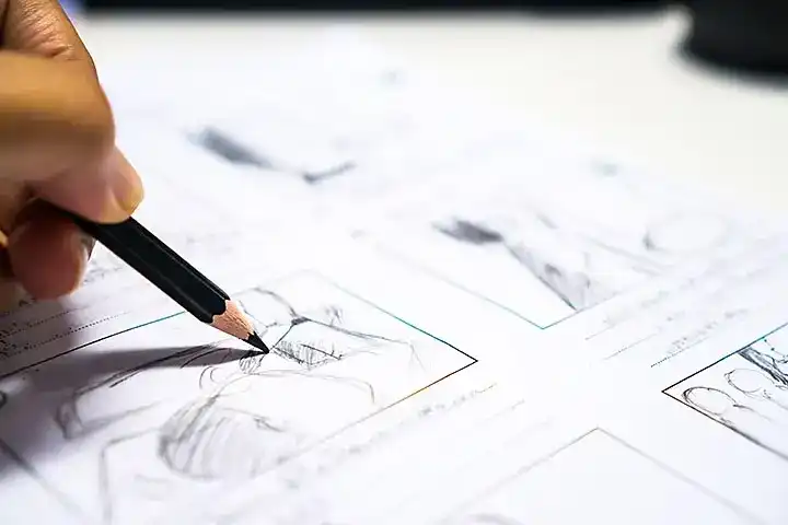 Close-up of a hand sketching storyboard panels with a pencil