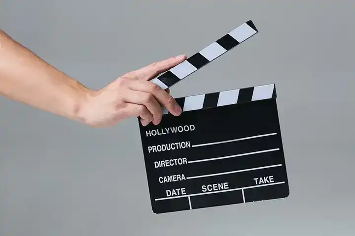 Hand holding a film clapperboard against a plain grey background.
