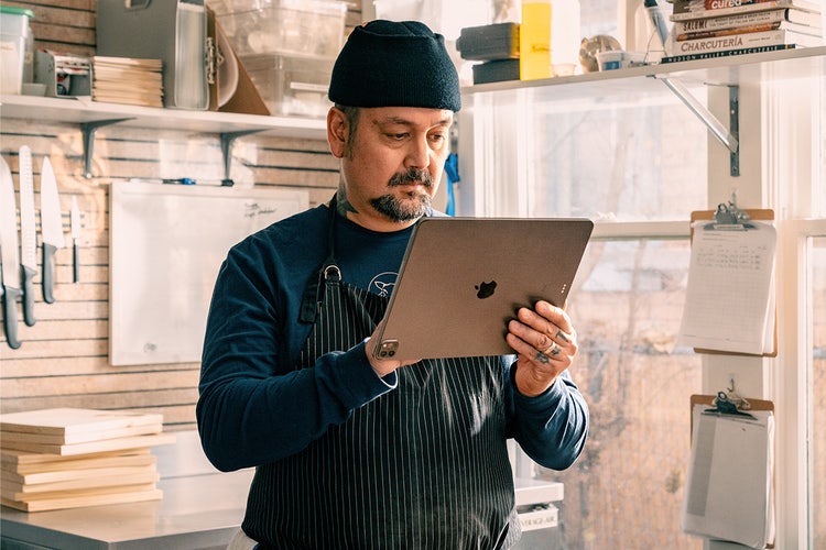 Man wearing black striped apron and hat in a shop holding an Apple tablet editing a printable fax cover sheet template.